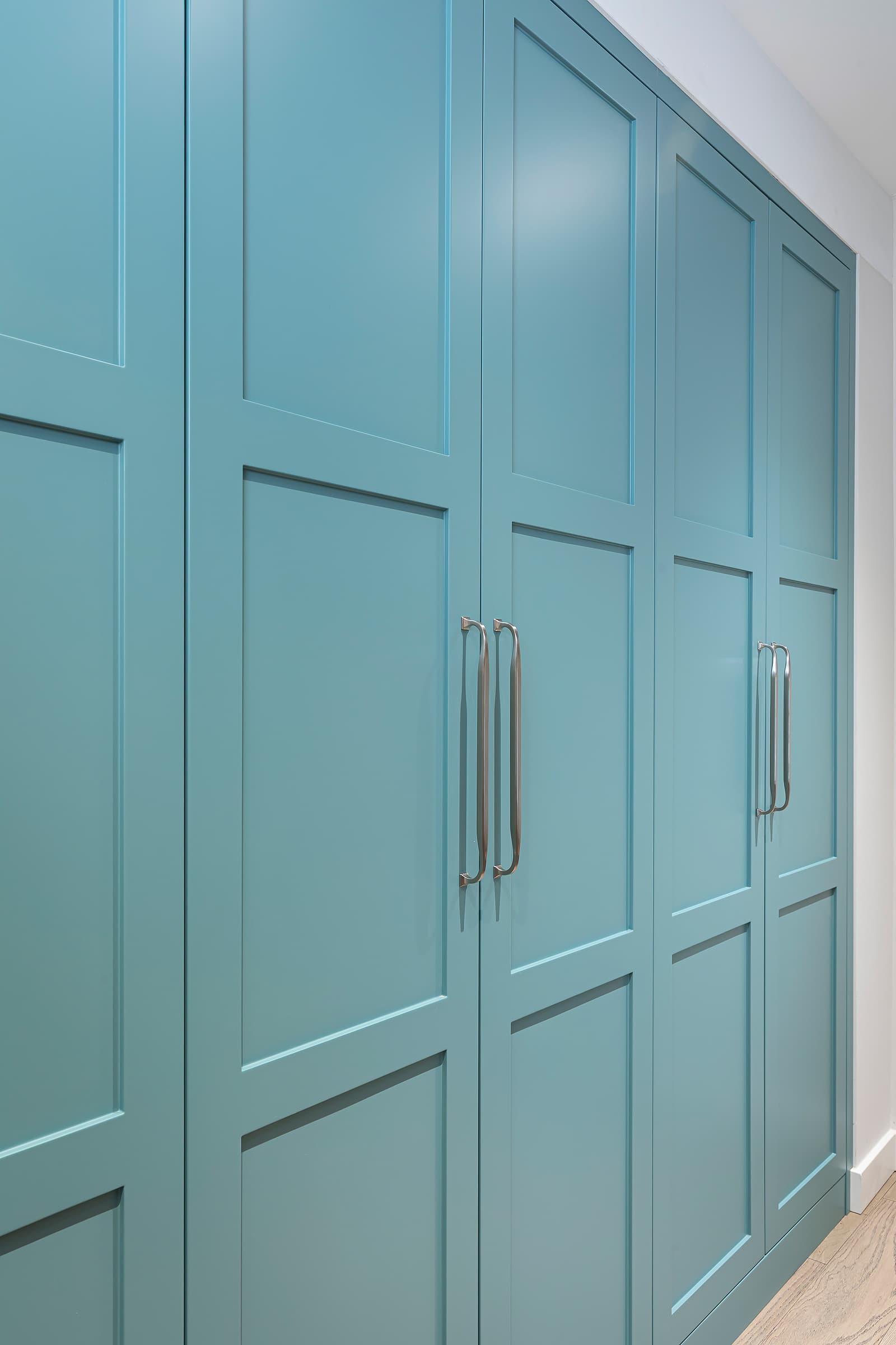 Angled view of teal shaker-style hallway cabinetry with brushed metal handles