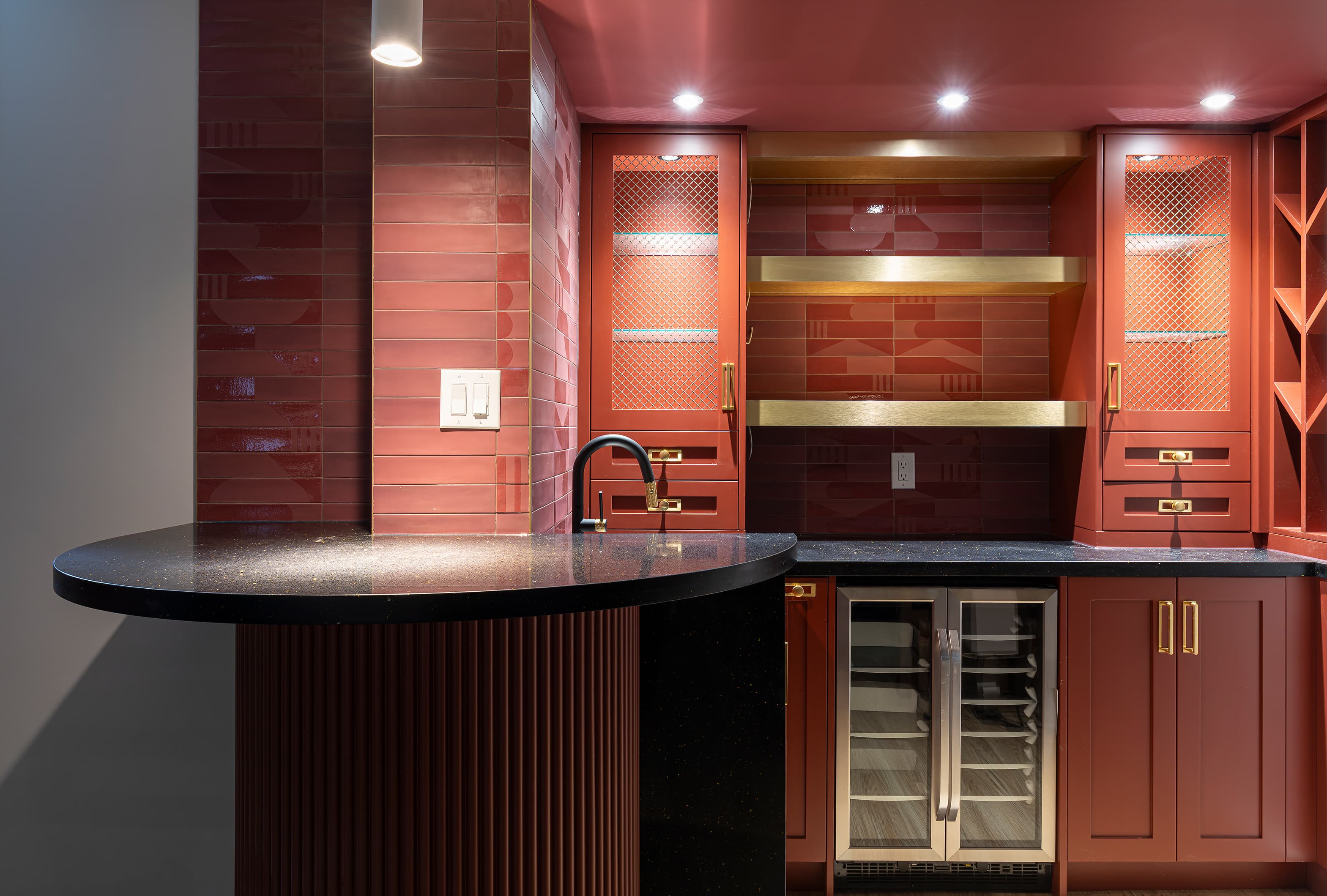 Modern home bar with burgundy cabinets, gold accents, black quartz countertop, and built-in wine fridge
